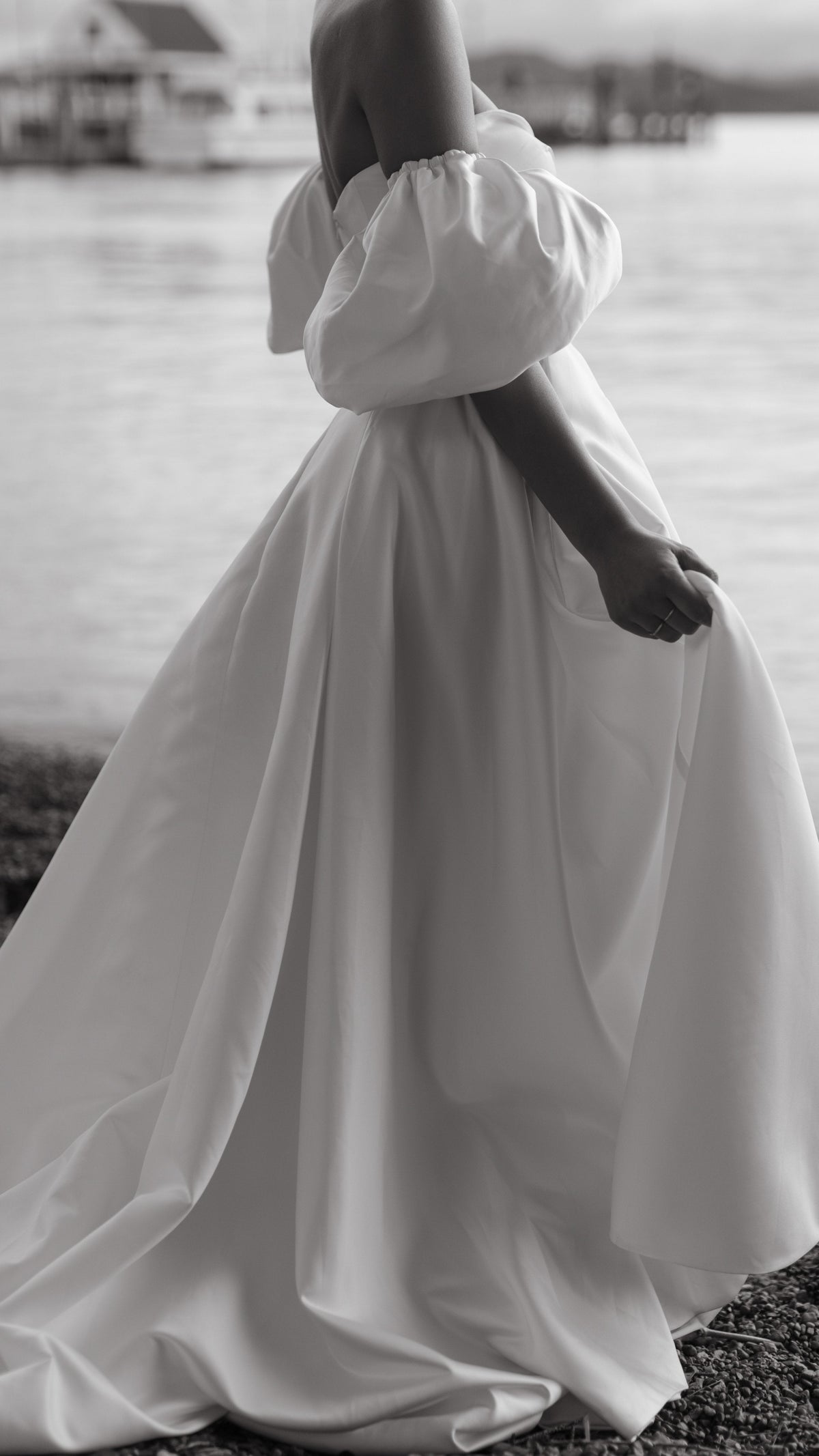Side crop of a satin wedding dress with a full skirt and puff sleeve, bride holding the fabric by the water, The Dark Side of The Moon