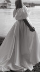 Side crop of a satin wedding dress with a full skirt and puff sleeve, bride holding the fabric by the water, The Dark Side of The Moon