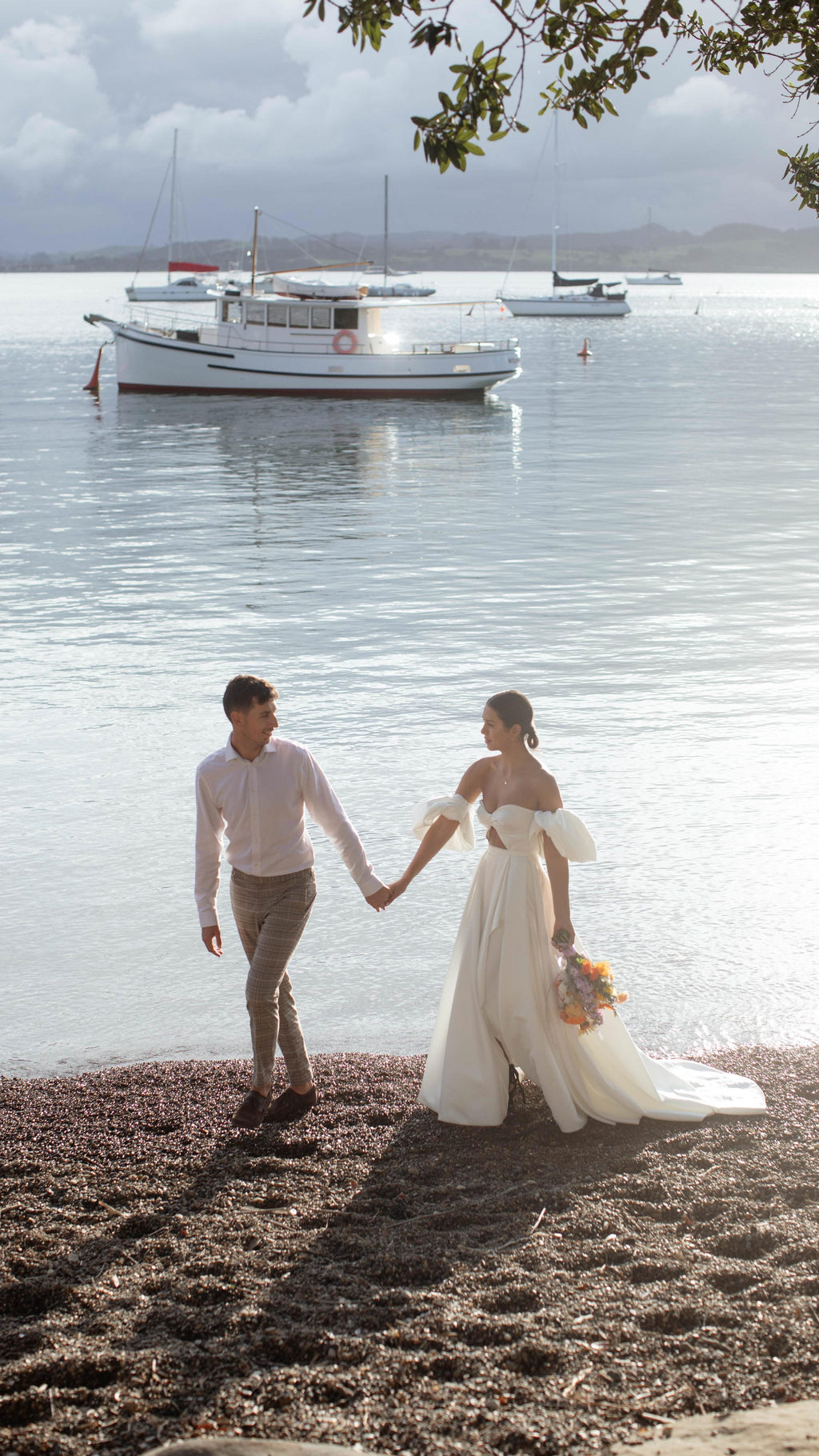 Couple holding hands on a sunny beach, bride in a satin wedding dress with puff sleeves and an orange bouquet, elopement, The Dark Side of The Moon