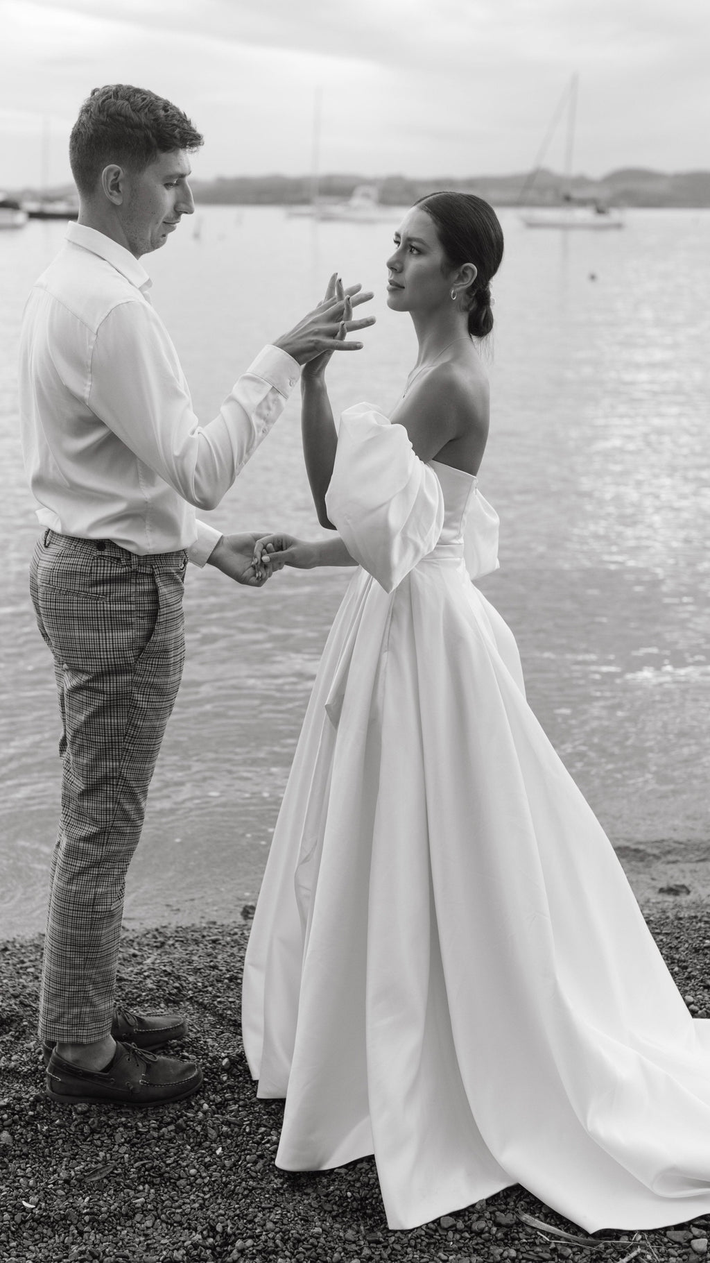 Couple facing each other on the shore, bride in a strapless satin wedding dress with puff sleeves raising her hand, The Dark Side of The Moon