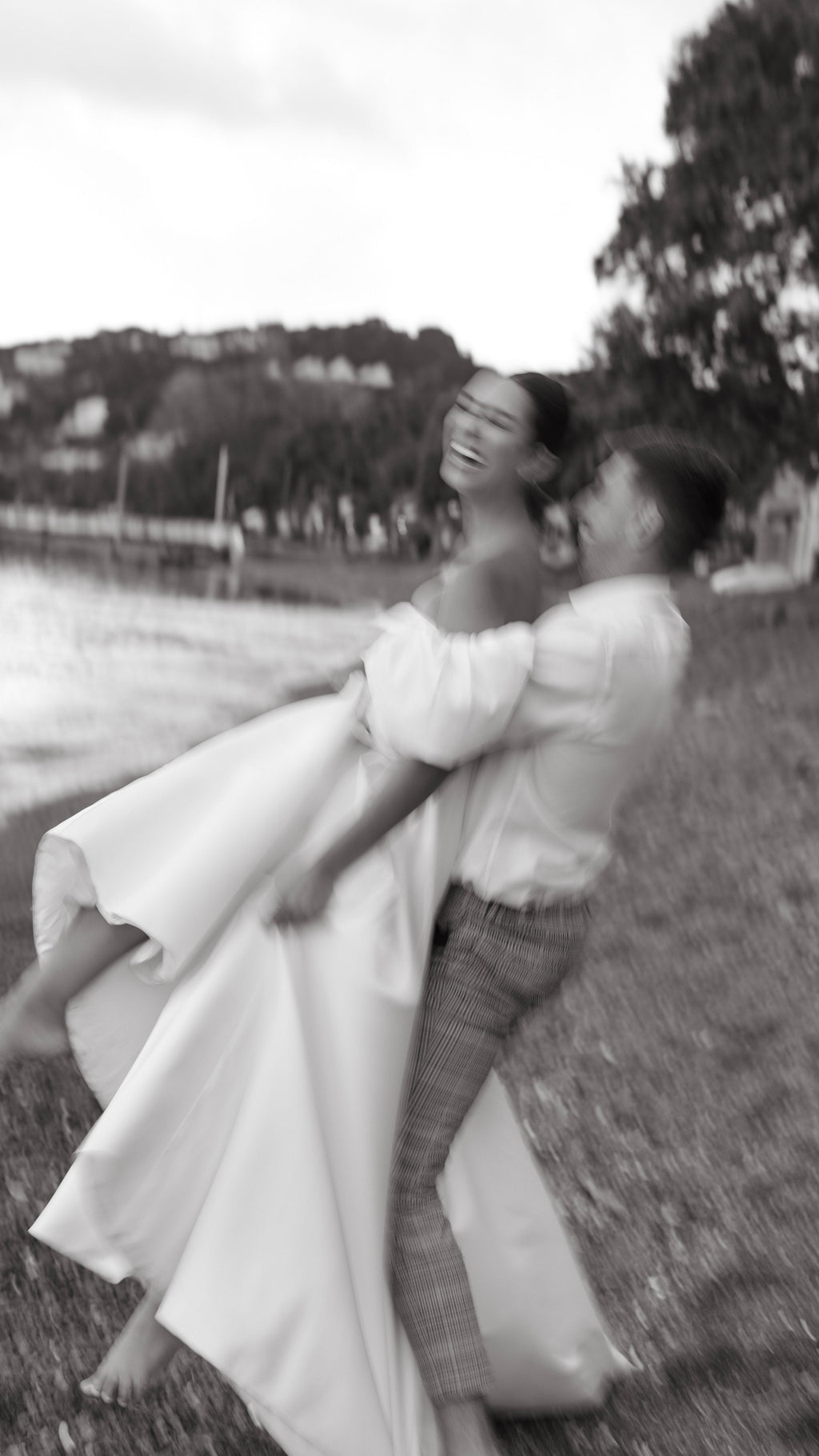 Groom lifting a laughing bride in a satin wedding dress with puff sleeves by the bay, soft motion blur, The Dark Side of The Moon