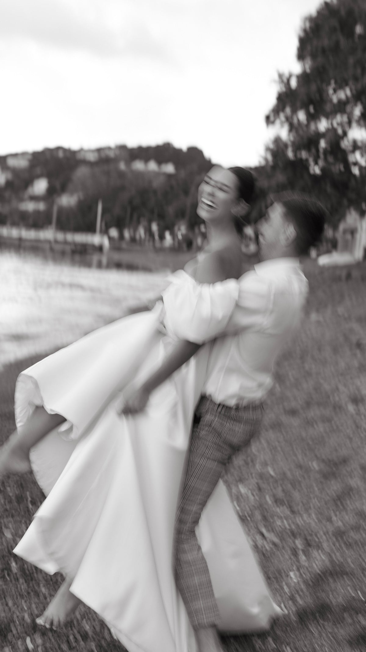 Groom lifting a laughing bride in a satin wedding dress with puff sleeves by the bay, soft motion blur, The Dark Side of The Moon