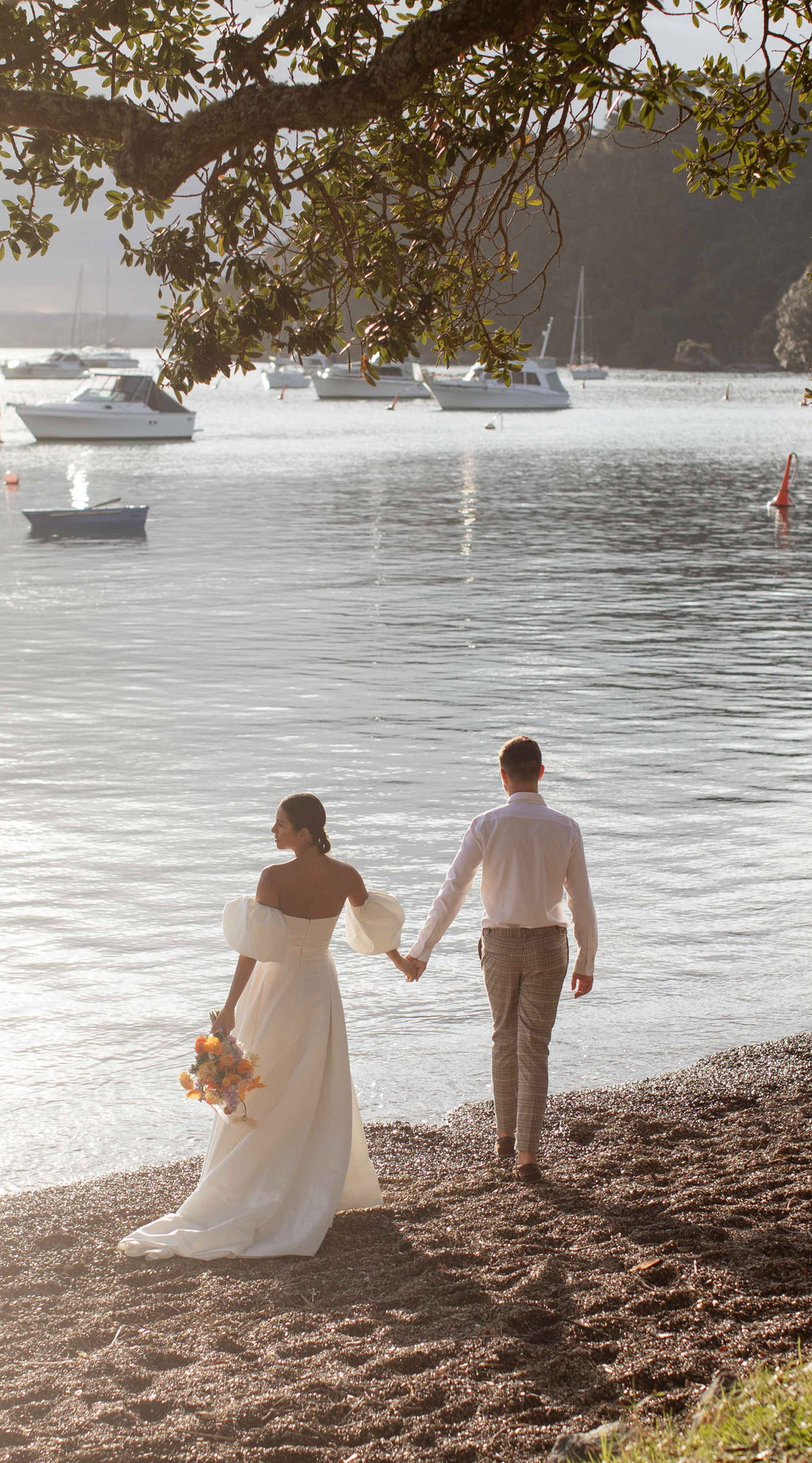 Back view of a couple walking to the water under a tree, bride in a satin wedding dress with puff sleeves, The Dark Side of The Moon