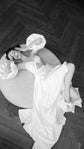 Overhead view of a bride lying on a round ottoman in a satin wedding dress with puff sleeves and a long skirt, The Dark Side of The Moon