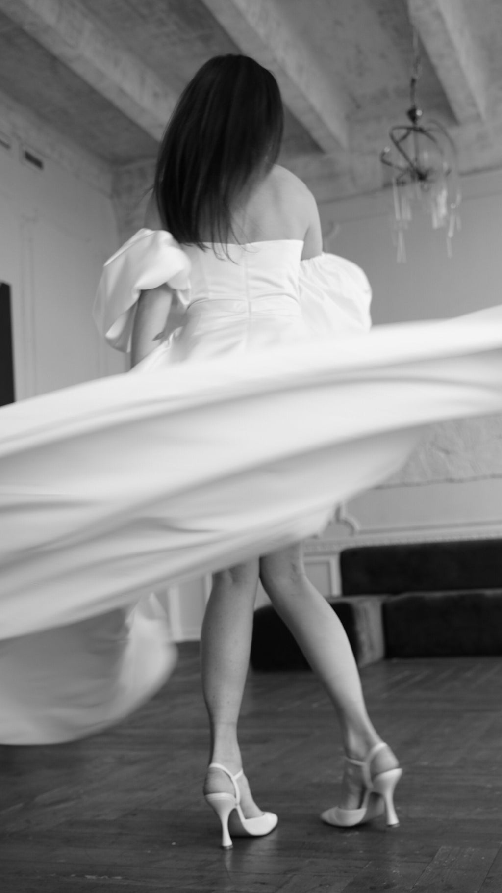 Back view of a satin wedding dress with puff sleeves mid-spin, the long skirt swirling above heeled shoes, The Dark Side of The Moon