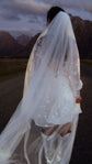 Back view of a short star reception dress through a long tulle veil, bride walking toward the mountains, Twilight Ivory