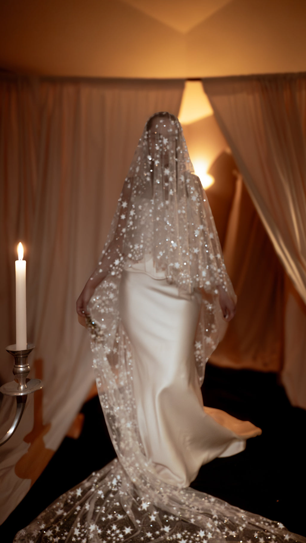 Bride under the blusher of a star-scattered wedding veil, satin gown and long tulle train glowing in candlelight, ethereal, Velum Veil