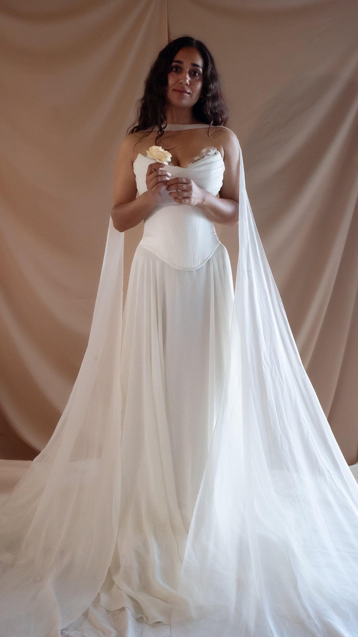 Bride holding a white rose in a strapless bridal corset with a long chiffon skirt and floor-length sheer sleeves, Venus Corset