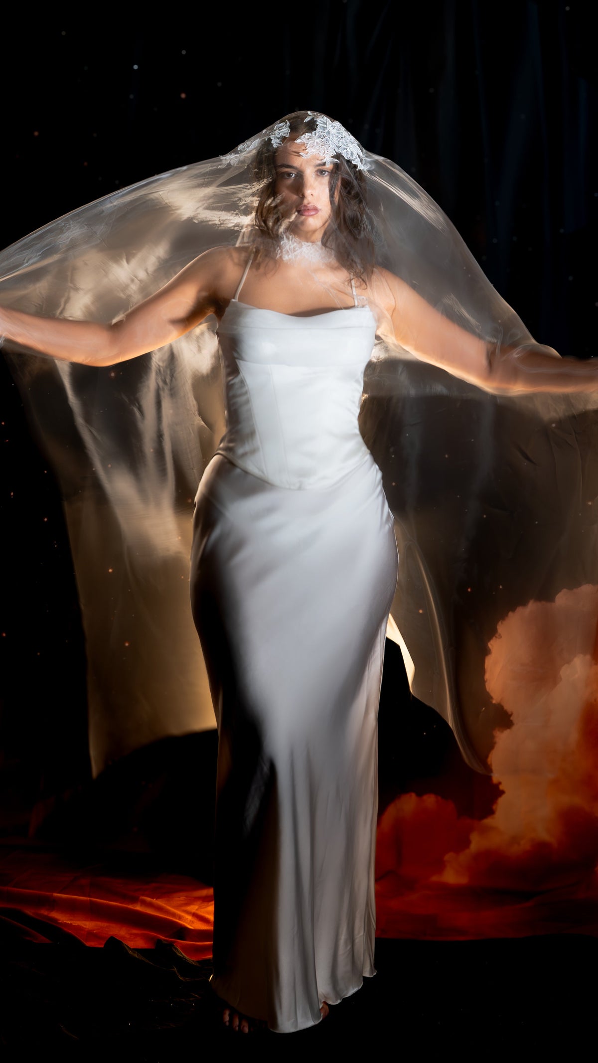 Super organza wedding veil with a Chantilly lace crown worn over the face, bride spreading the veil wide against a dark backdrop, Vespera by Ephemeris