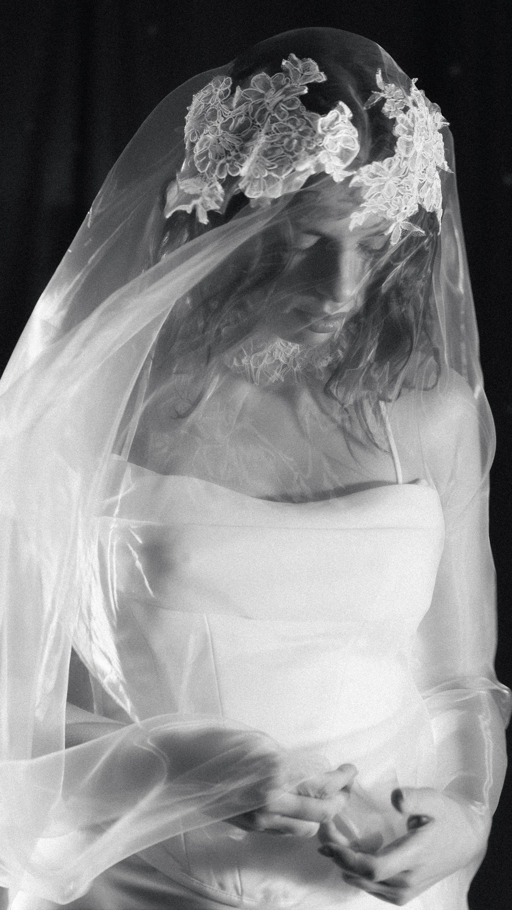 Black and white portrait of a bride looking down under a lace crown wedding veil, organza draped over her hands, mantilla veil, Vespera
