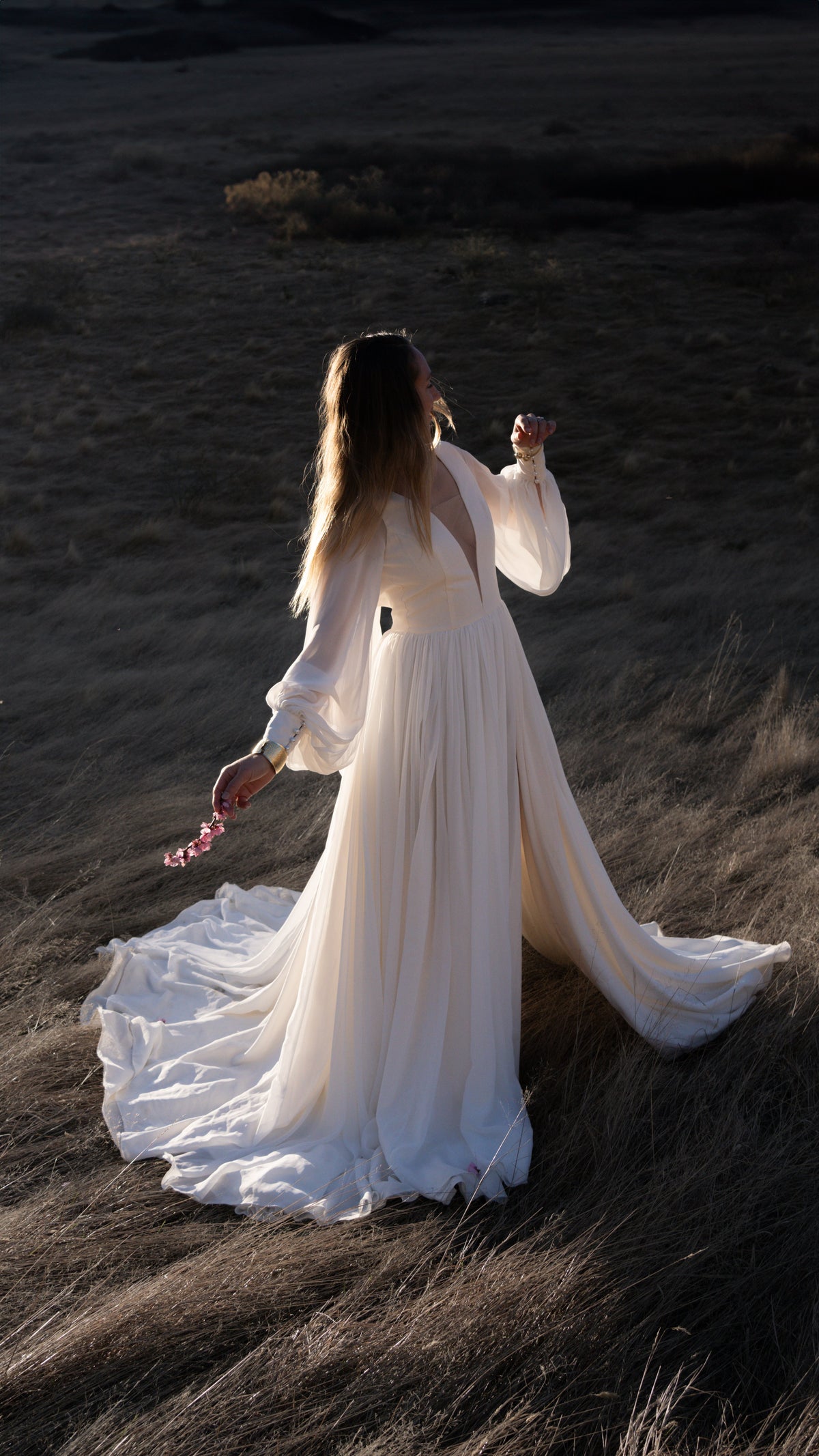 Chiffon sample wedding dress with sheer long sleeves, slit and train, bride in a dark meadow holding flowers, When the Moon is Out Sample by Ephemeris