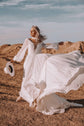 Bride flinging the chiffon skirt of a long-sleeve sample wedding dress into the wind on a desert ridge, hat in hand, When the Moon is Out Sample