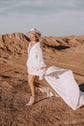 Bride in a hat and ankle boots striding through dunes, chiffon sample wedding dress with a plunging V and flying train, When the Moon is Out Sample