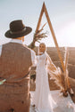 Couple at a wooden triangle arch with pampas grass, bride in a long-sleeve chiffon sample wedding dress facing the groom, elopement, When the Moon is Out Sample