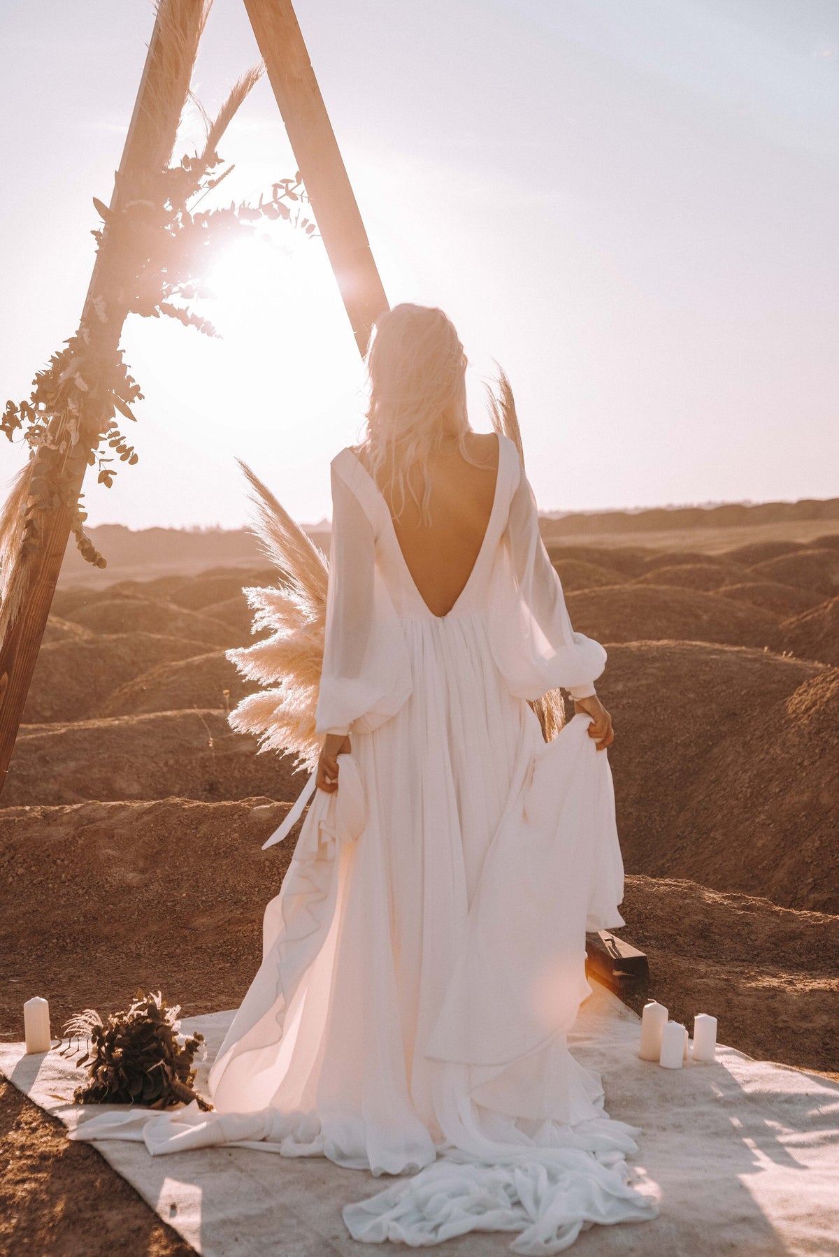 Back view of an open-back chiffon sample wedding dress under a triangle arch at sunset, candles on a rug, When the Moon is Out Sample