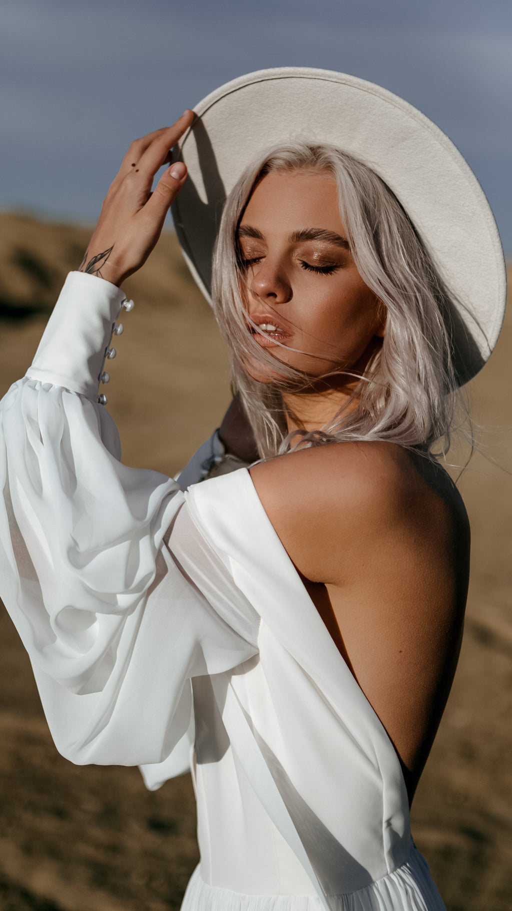 Close portrait of a bride holding her hat brim, plunging chiffon sample wedding dress with a buttoned balloon sleeve, When the Moon is Out Sample