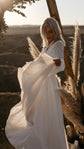 Backlit bride swirling the chiffon skirt of a long-sleeve sample wedding dress beside pampas grass at golden hour, When the Moon is Out Sample