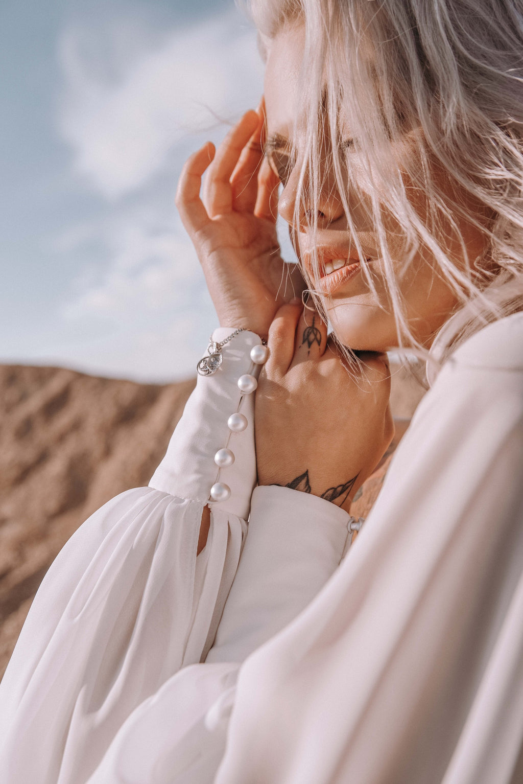 Close crop of a bride shielding her face in the wind, chiffon sample wedding dress sleeve with a buttoned cuff, sky behind, When the Moon is Out Sample