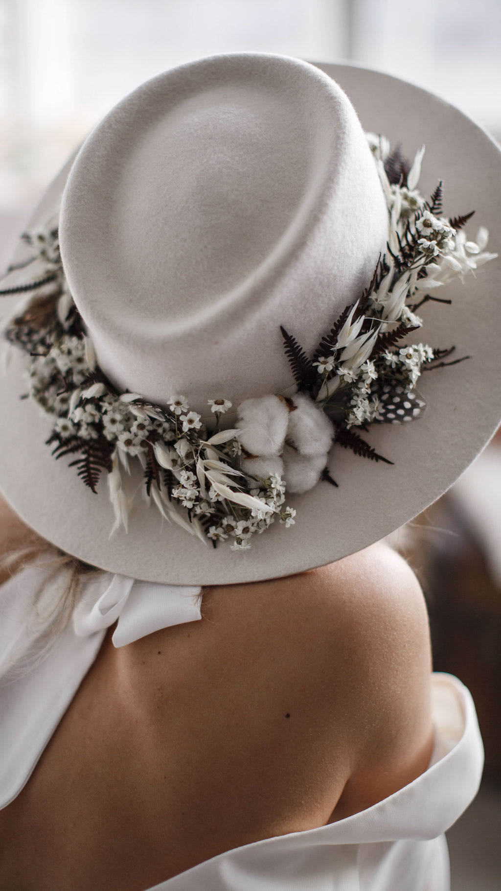 Close detail of the neck tie at the back of a chiffon wedding dress under a felt hat, bare shoulder in soft light, When the Moon is Out