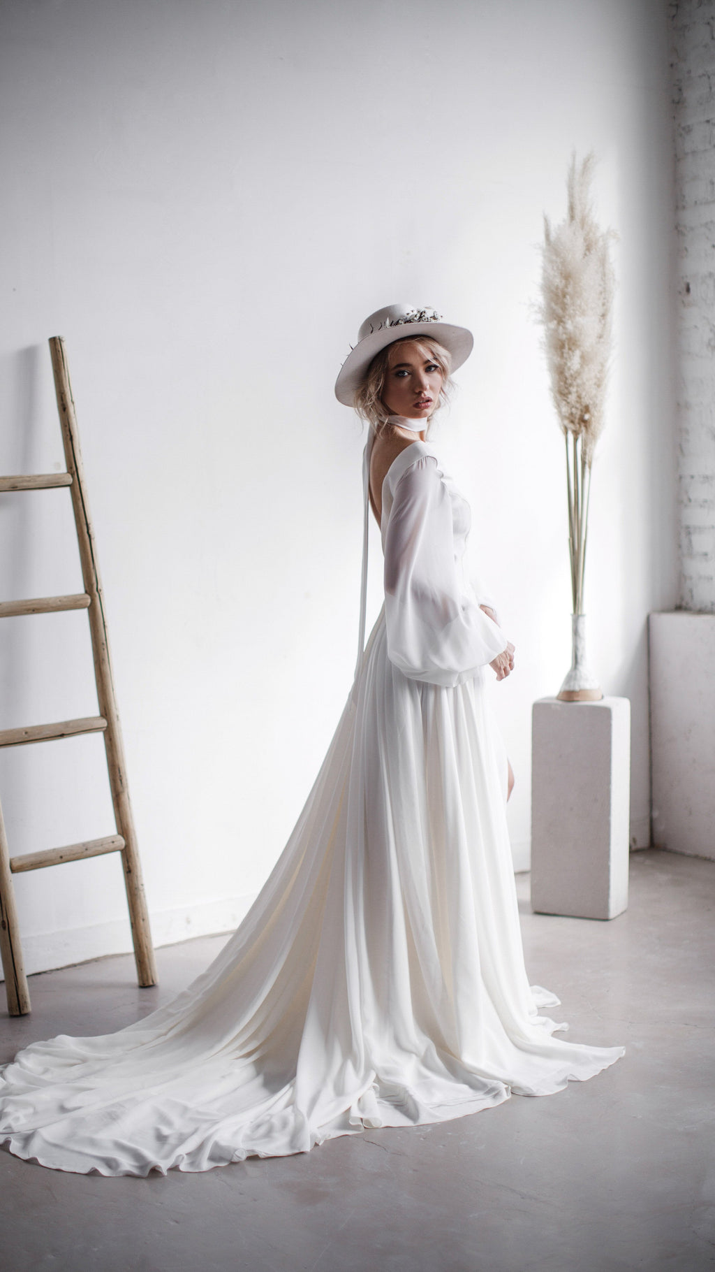 Side view of a bride by a ladder in a long-sleeve chiffon wedding dress, the train swirling across the concrete floor, When the Moon is Out