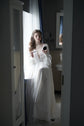 Bride getting ready by a bathroom mirror in a long-sleeve chiffon wedding dress with a plunging V neckline, When the Moon is Out