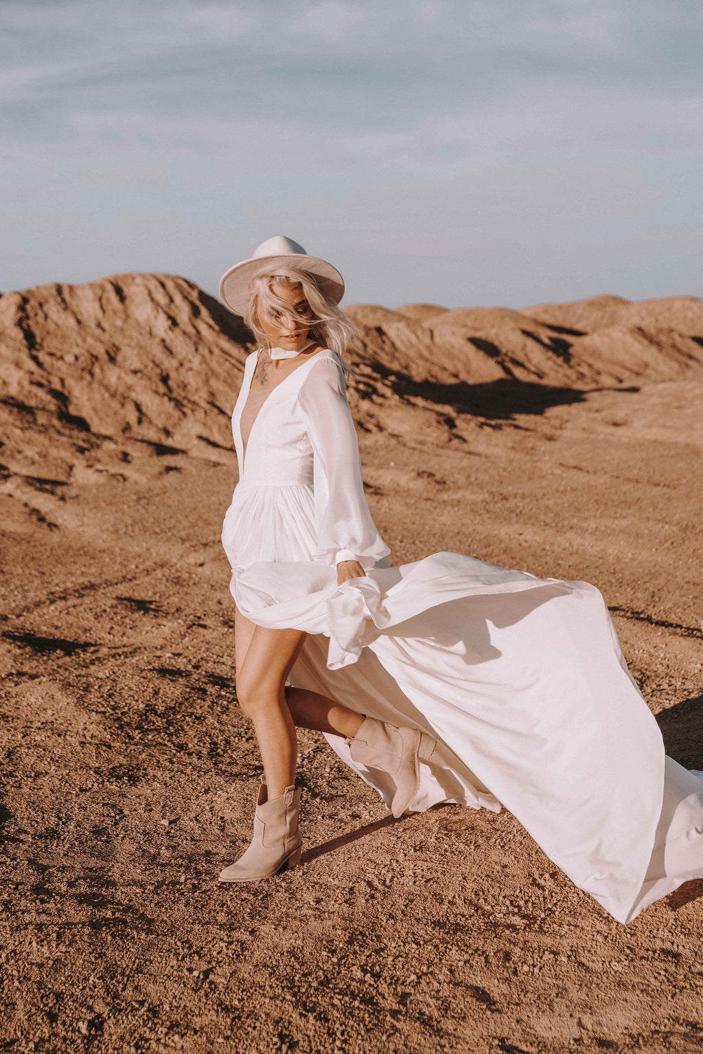 Bride in a hat and ankle boots striding through dunes, chiffon wedding dress with a plunging V and flying train, When the Moon is Out
