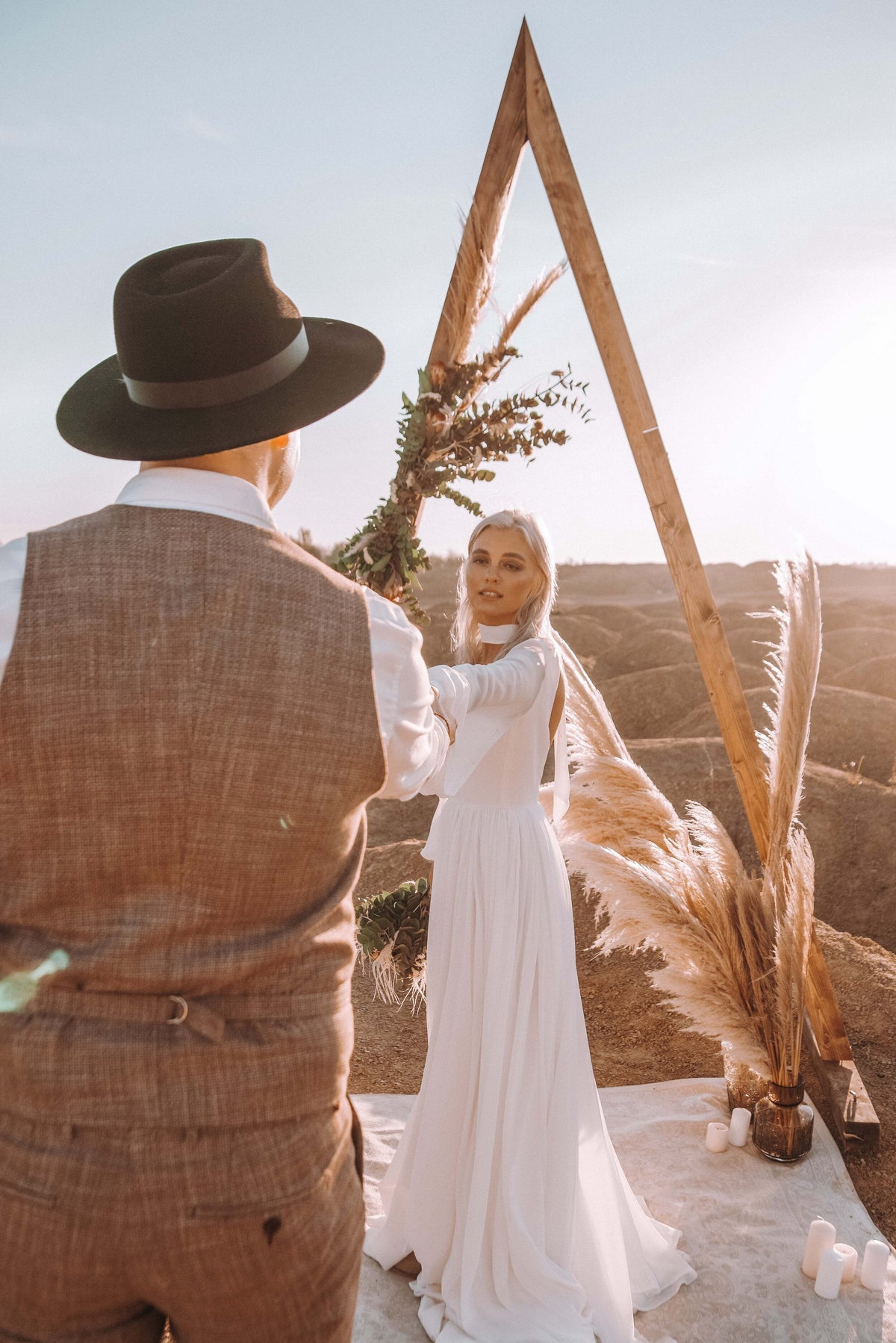 Couple at a wooden triangle arch with pampas grass, bride in a long-sleeve chiffon wedding dress facing the groom, elopement, When the Moon is Out