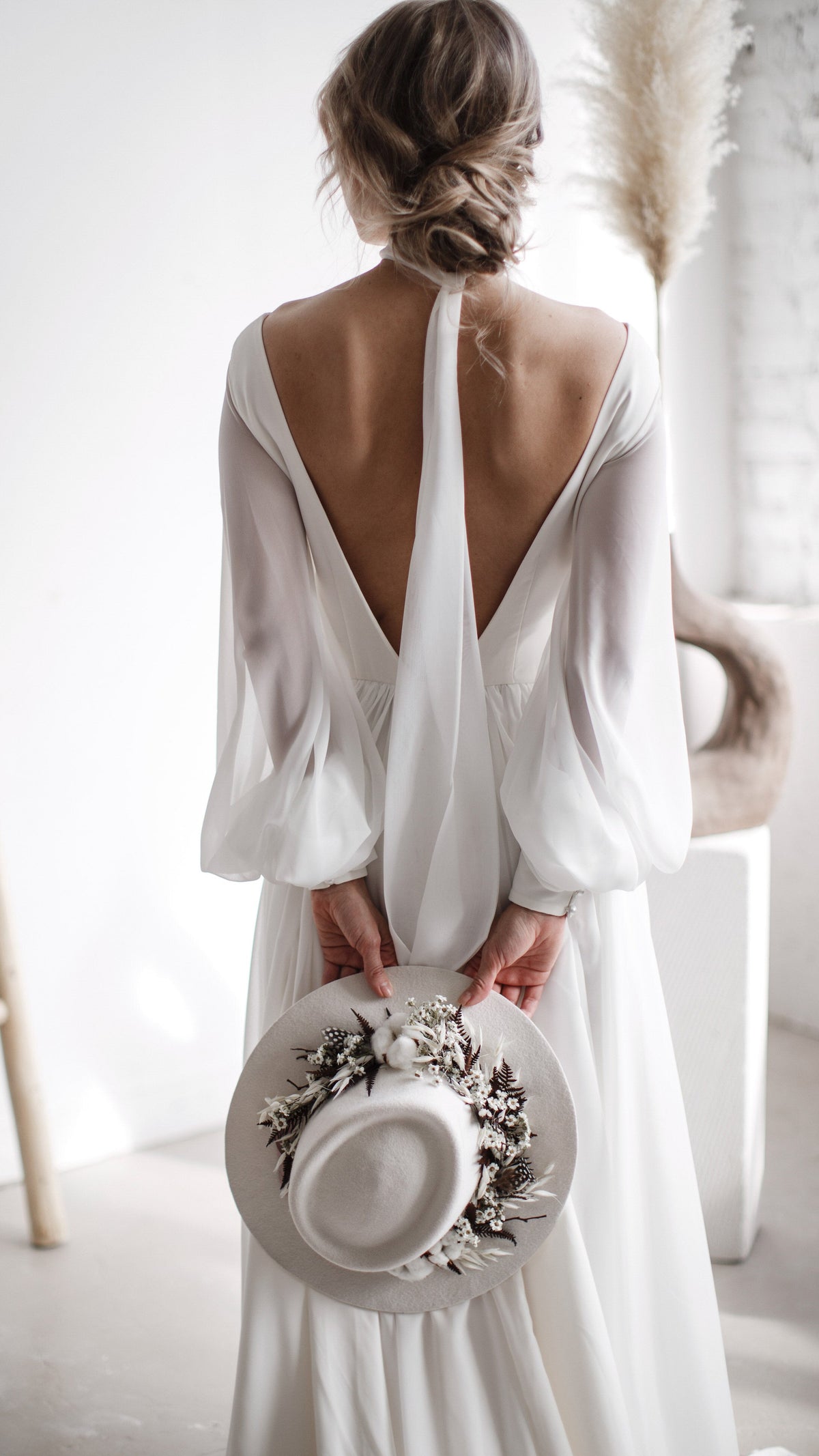 Back view of a chiffon wedding dress with a deep V back and the scarf trailing down the spine, bride holding a hat, When the Moon is Out