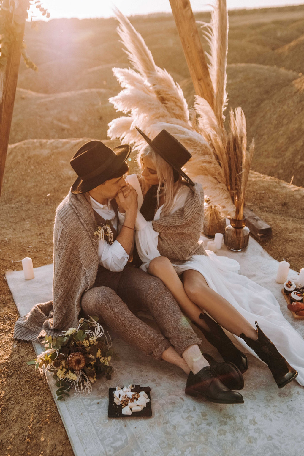 Couple sitting on a rug with pampas and candles, bride in a chiffon wedding dress with a knit wrap and boots, When the Moon is Out