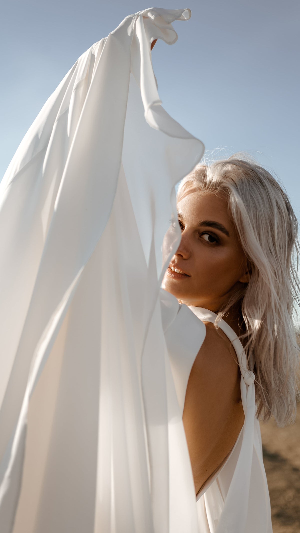 Bride raising a long chiffon sleeve that billows in the wind, open back of the wedding dress in sunlight, When the Moon is Out