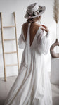 Back view of an open-back wedding dress in chiffon, scarf falling from the neck, bride touching her hat by a ladder, When the Moon is Out
