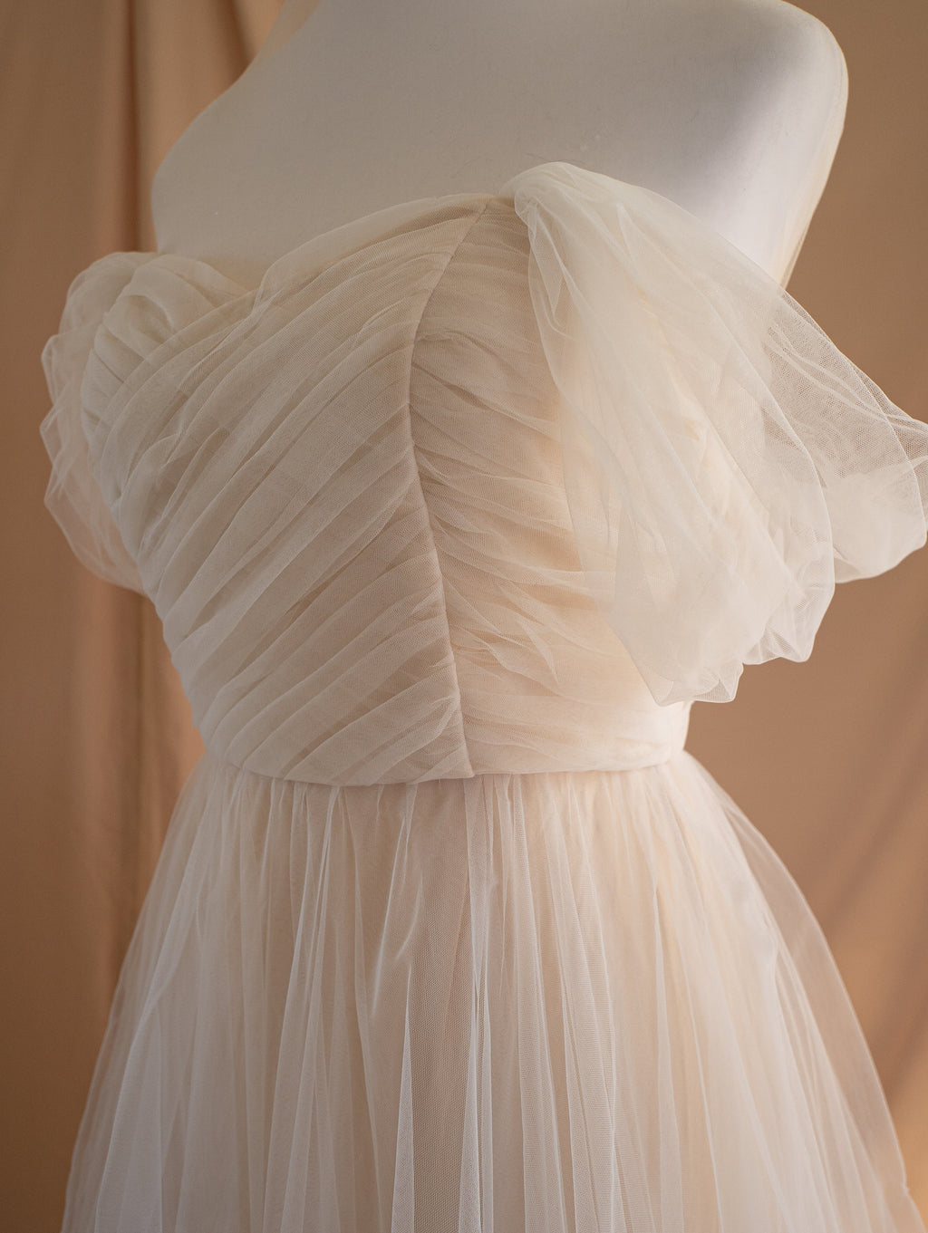 Angled close-up of the pleated champagne tulle bodice and puffed off-shoulder sleeves of a sample wedding dress, Whisper Sample
