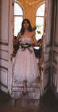Model stepping through tall doors in a midi star wedding dress with straps and a black jewelled bow at the waist, Wild Stars