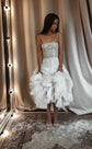 Model lifting the ruffled tulle hem of a star corset wedding dress with straps, curtain backdrop and rug, Wild Stars