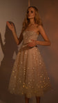 Strapless corset wedding dress with a midi tulle skirt covered in reflective stars glowing under warm light, model by a wall, Wild Stars