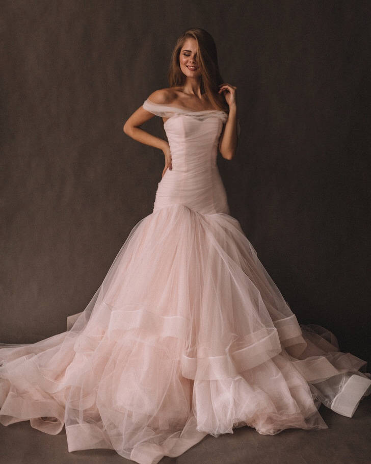 Front view of a blush tulle wedding dress with off-shoulder straps, draped bodice and layered train, Peony