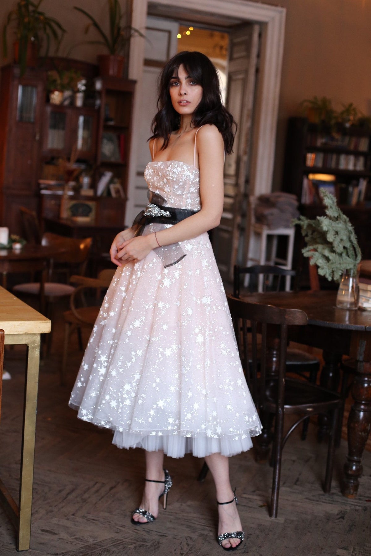 Model in a cafe in a strappy corset wedding dress with a full star tulle midi skirt and a black bow sash, Wild Stars