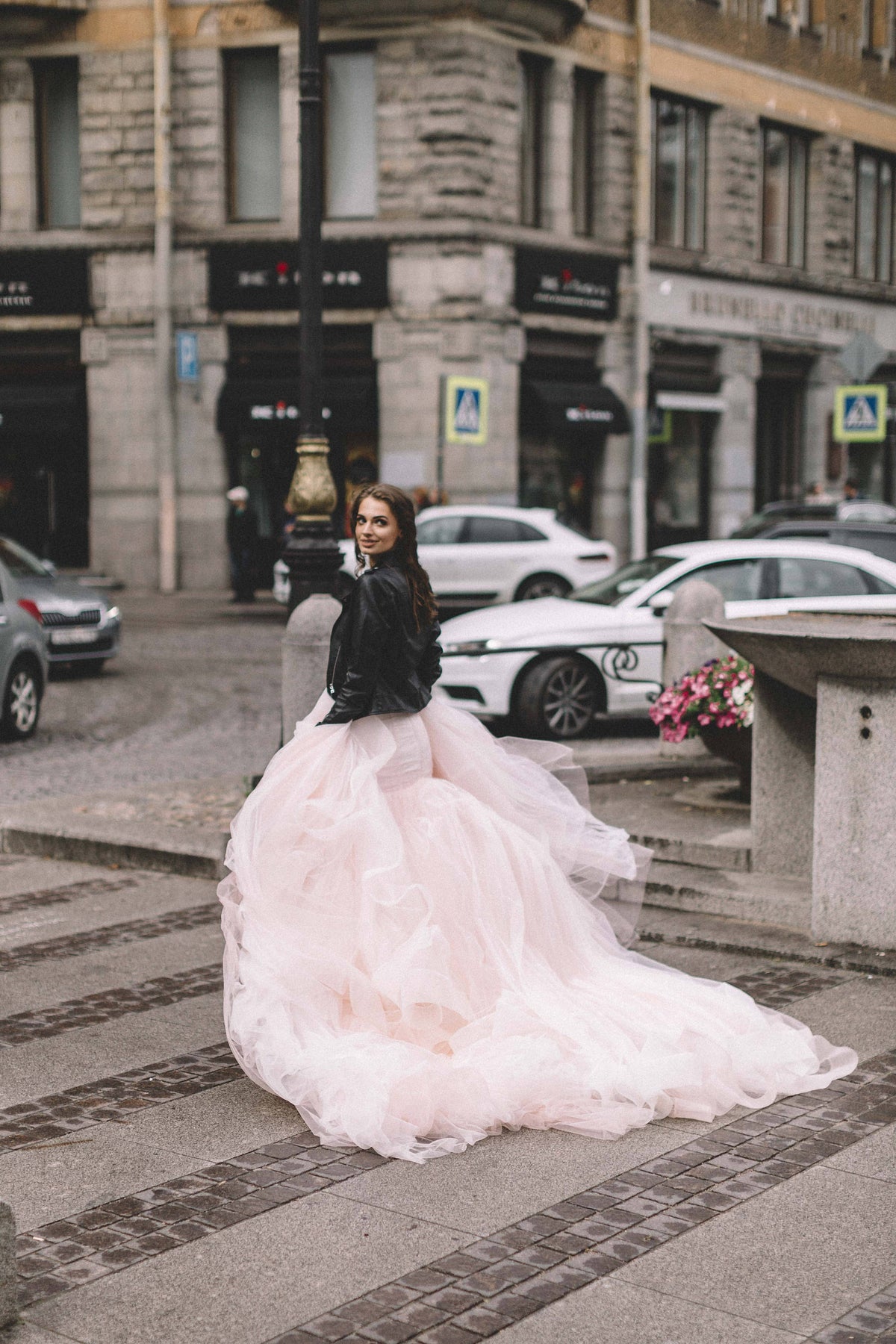 Blush tulle wedding dress with a leather jacket, bride looking back across a city square, long train, Peony