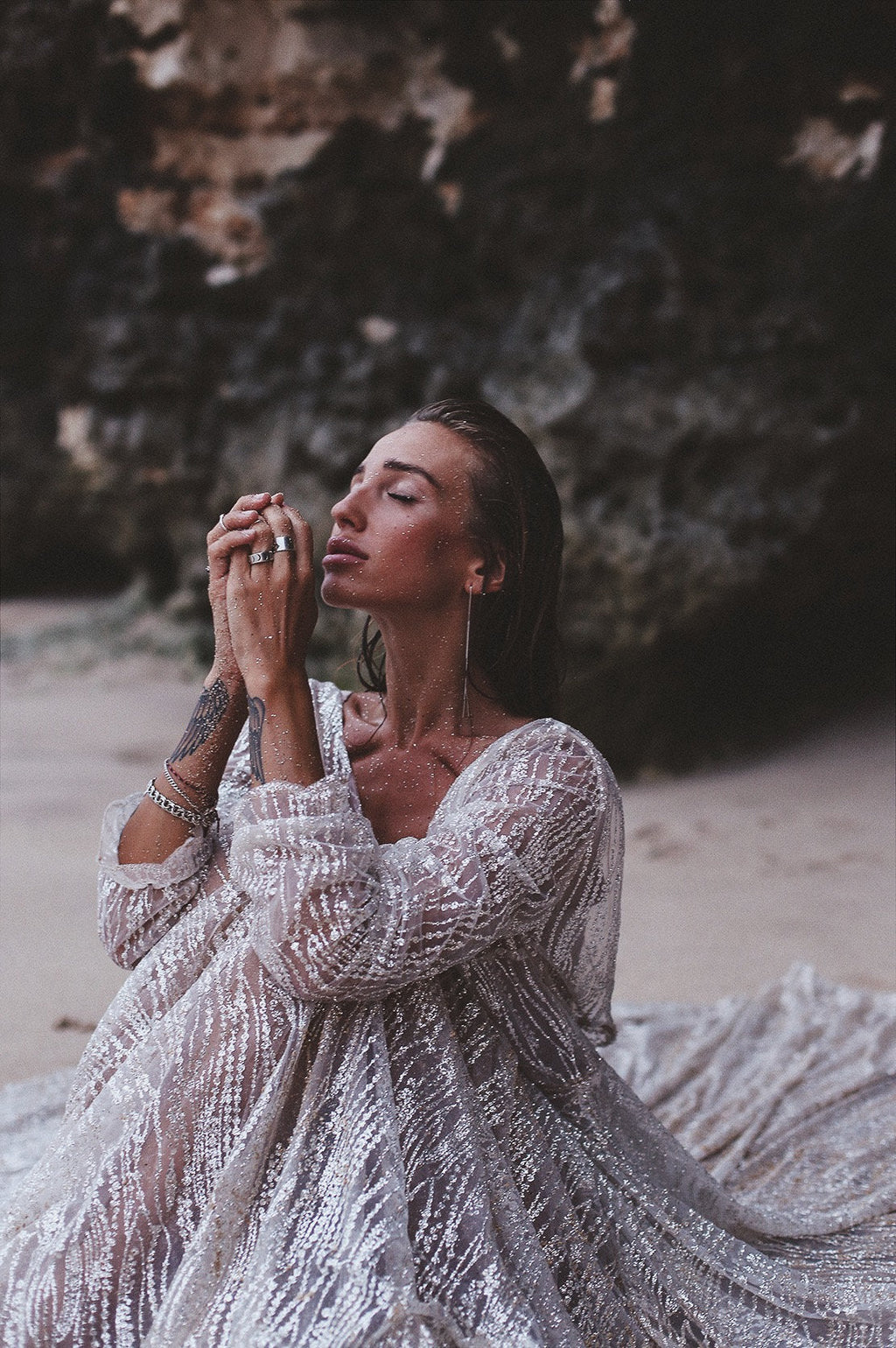 Close crop of a bride seated on the sand, sheer glitter lace sleeves and full skirt of an ivory wedding dress, Galaxy Ivory