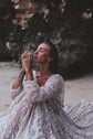 Close crop of a bride seated on the sand, sheer glitter lace sleeves and full skirt of an ivory wedding dress, Galaxy Ivory