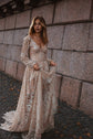Bride lifting the skirt of a champagne lace wedding dress on cobblestones by a stone wall, train swept behind, Galaxy Champagne