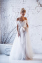 Model looking down in a pleated tulle sample wedding dress with off-shoulder drape, white brick and branches, ethereal, Whisper Sample