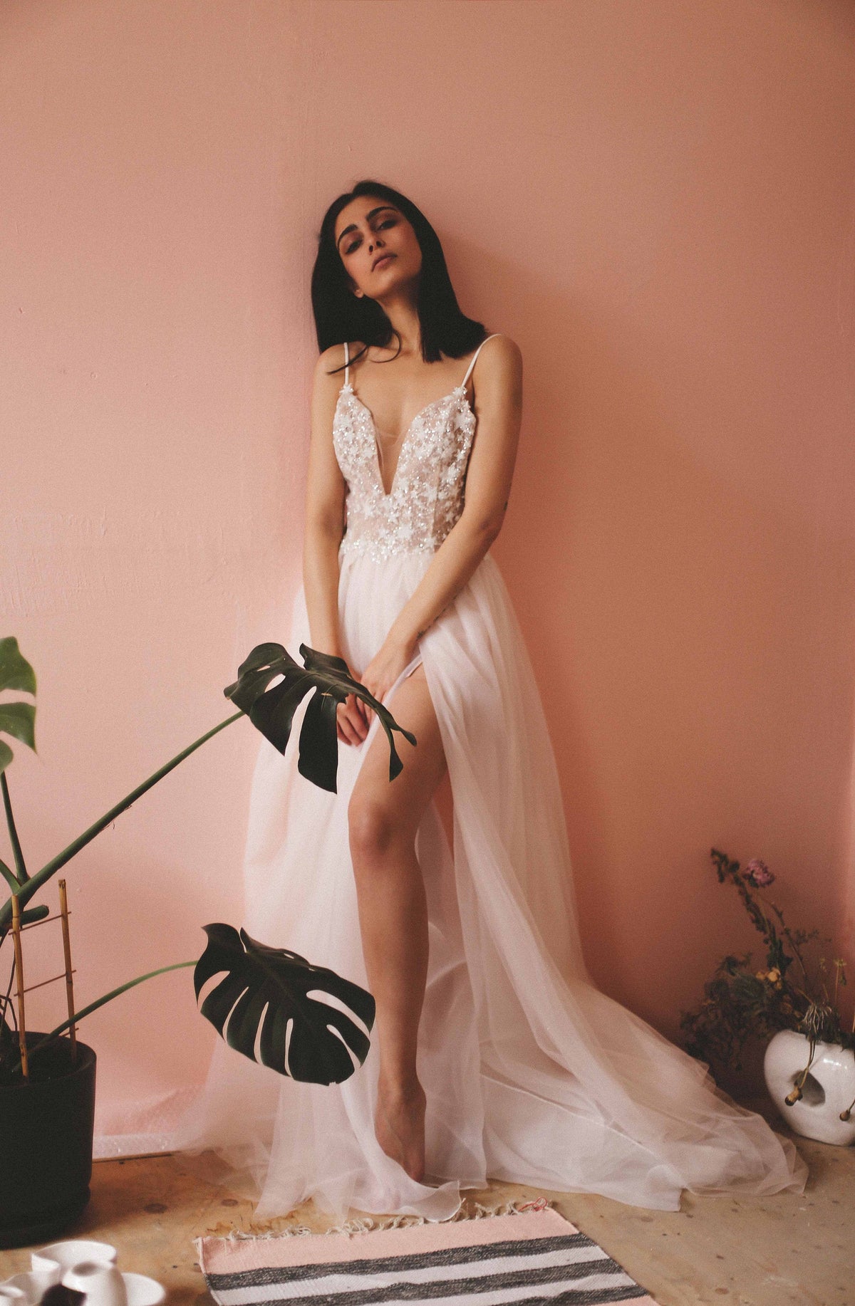 Bride against a pink wall holding a monstera leaf, sparkly plunge neck wedding dress with a side slit, Make a Wish