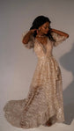 Full-length champagne wedding dress with the floor-length overskirt sweeping into a train, model touching her hair, Soleil