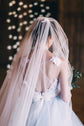 Back view of a raw-cut tulle wedding veil falling over an open lace back, soft bokeh lights in a wooden barn, Cascade Veil