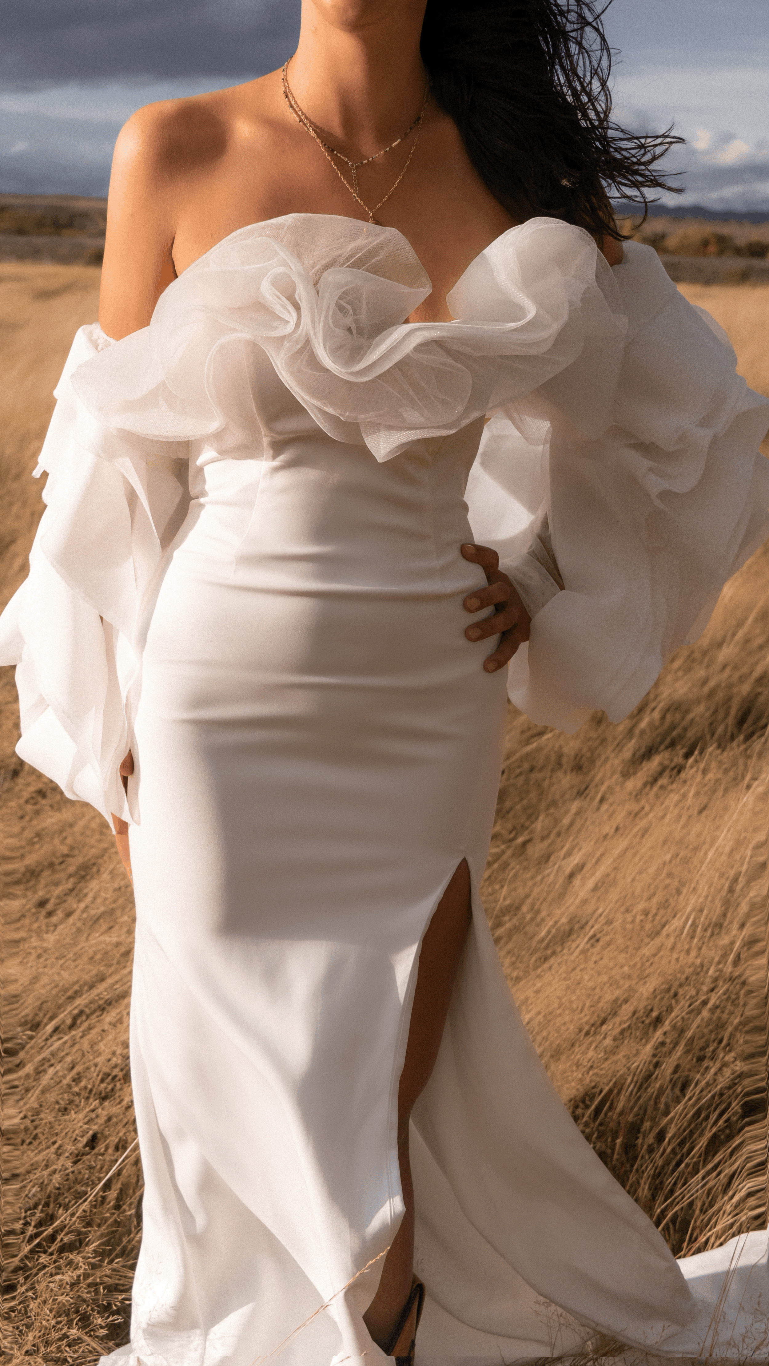 Close crop of sculptural petal detachable sleeves framing a strapless crepe gown, hand on hip, windy field, My Darling Hurricane Sleeves