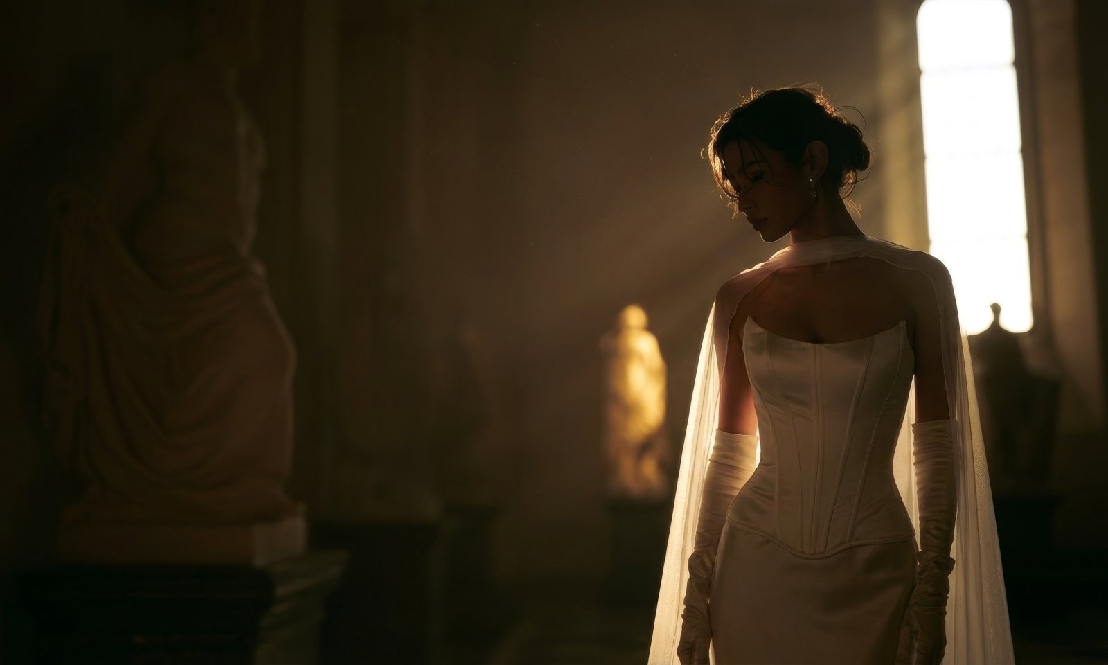 A bride in a corseted gown stands in a sunlit hall
